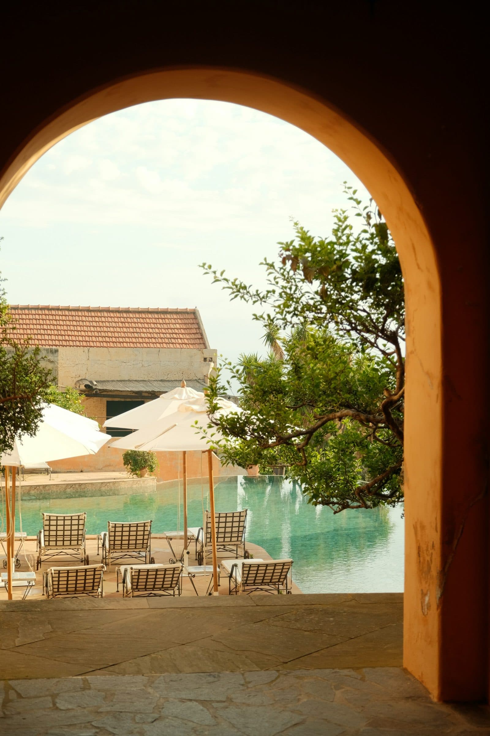 A stone archway framing a pool with a sea view.