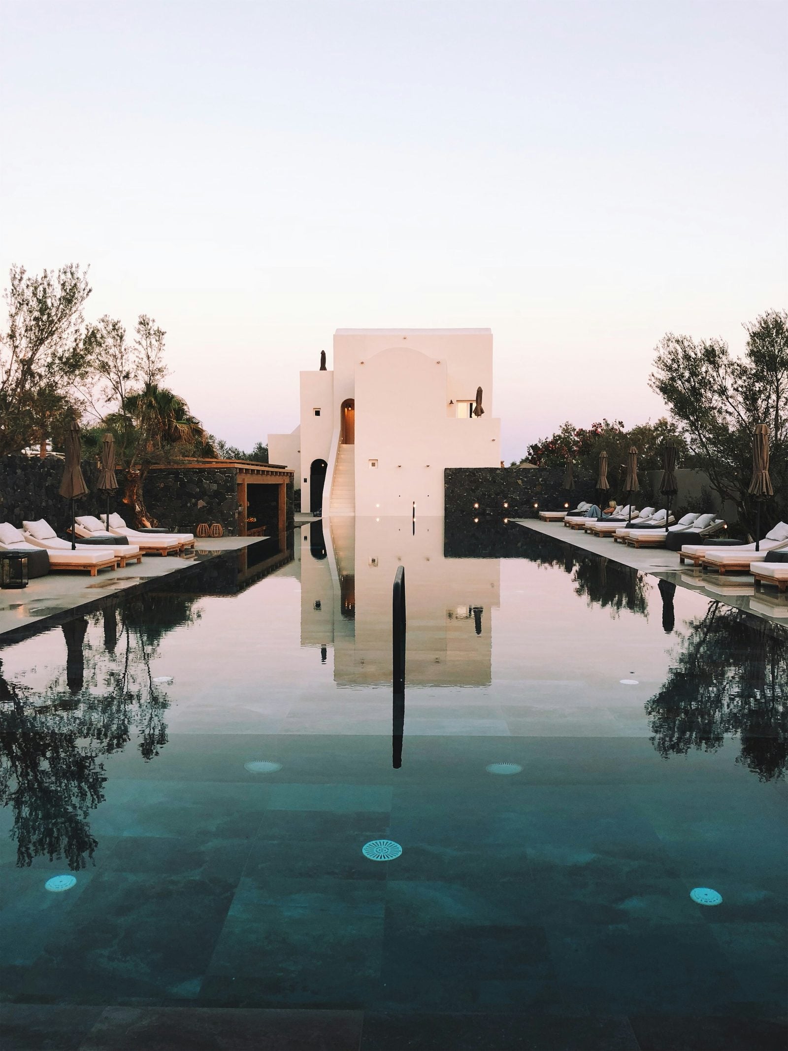A white Mediterranean building at dusk, reflected in a dark, still pool.