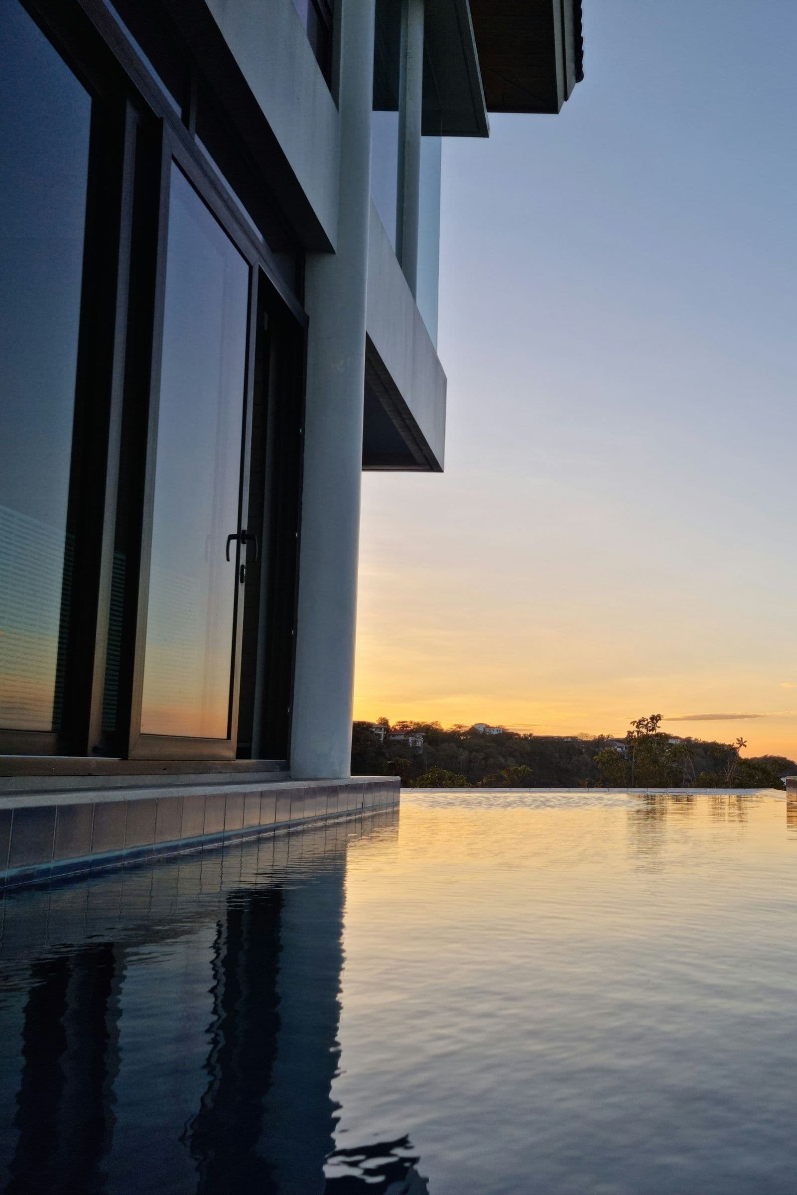 Ein Infinity-Pool neben einer modernen Villa, in dem sich der Sonnenuntergang über dem Meer spiegelt.