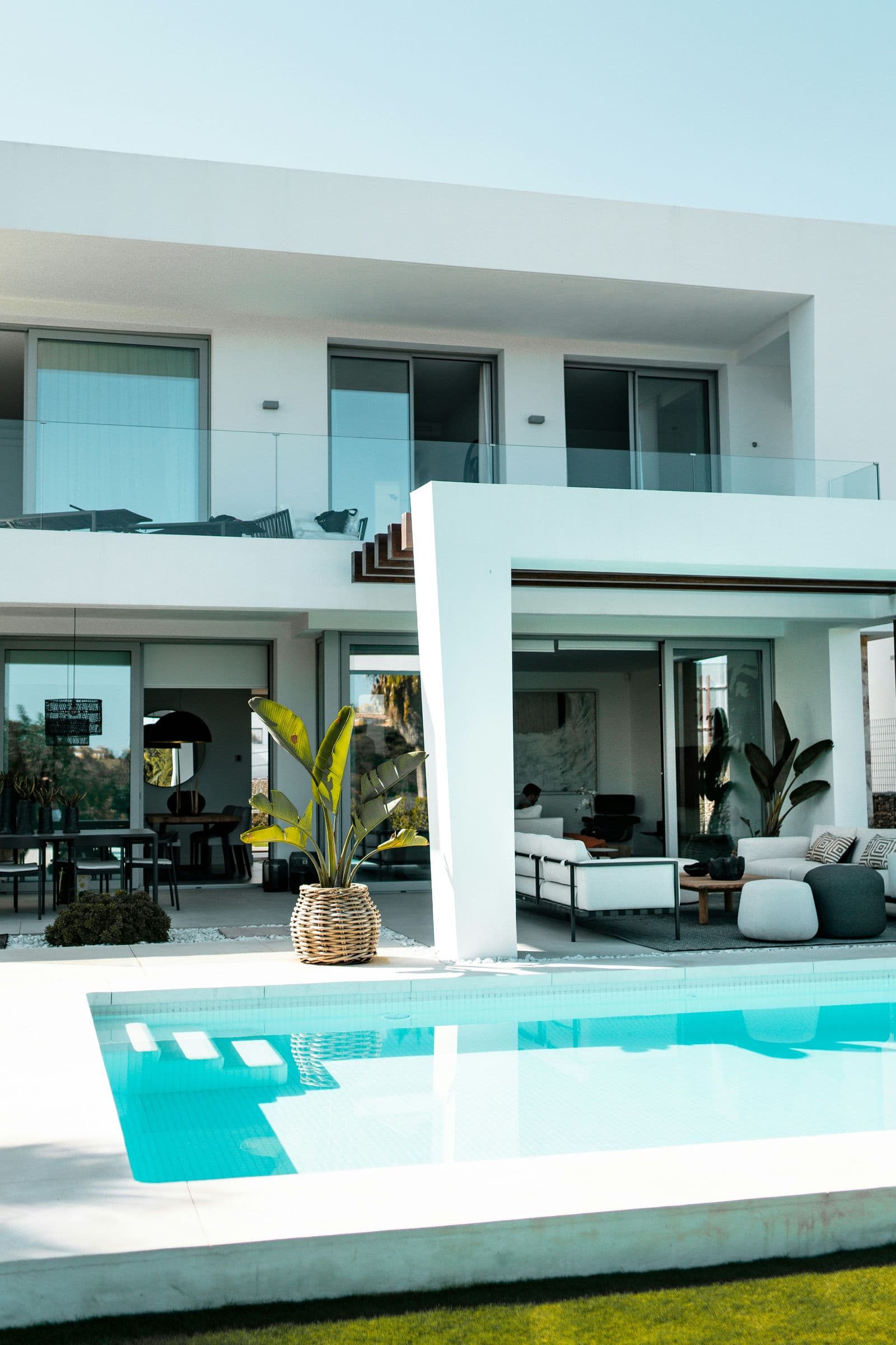 Eine moderne weiße Villa mit Pool, Palmen und Rasen unter klarem Himmel.